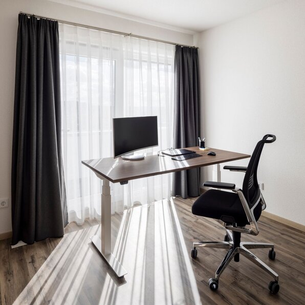 Modernes Homeoffice in einem FingerHaus mit Schreibtisch, Bürostuhl und großem Fenster mit Vorhängen.