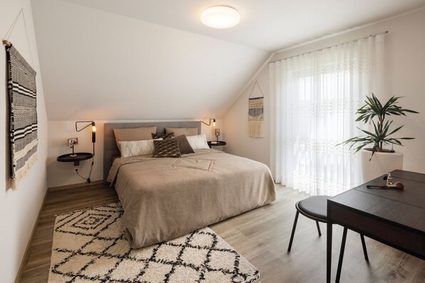 Schlafzimmer im Musterhaus VIO Köln mit gemütlichem Doppelbett, warmen Holzakzenten und dekorativen Textilien.