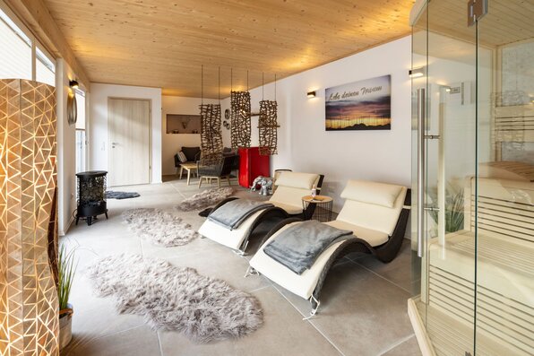 Moderner Wellnessraum mit Sauna, Relaxliegen, Hängesesseln und gemütlicher Beleuchtung.
