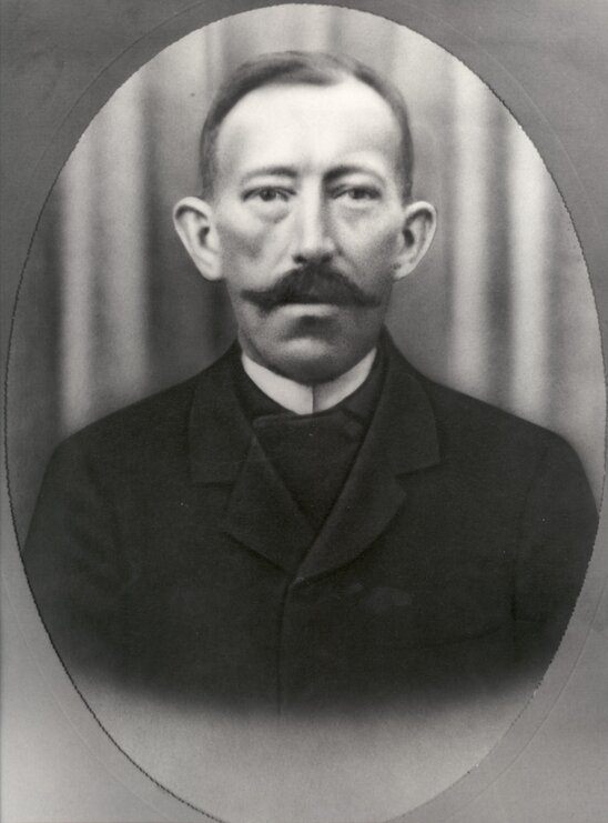 Porträt eines Mannes in dunklem Anzug vor einem Vorhang in einem ovalen Rahmen. - Gründer Heinrich Finger