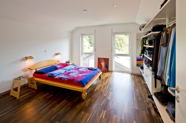 Modernes Schlafzimmer in einem frei geplanten Finger-Haus mit Doppelbett, Holzfußboden, offener Kleideraufbewahrung und Zugang zum Balkon.