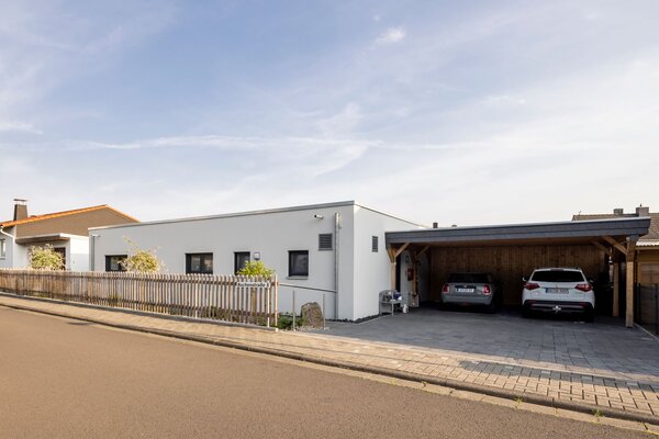 Modernes eingeschossiges Flachdachhaus mit Carport, Holzzaun und gepflasterter Einfahrt in einem Wohngebiet