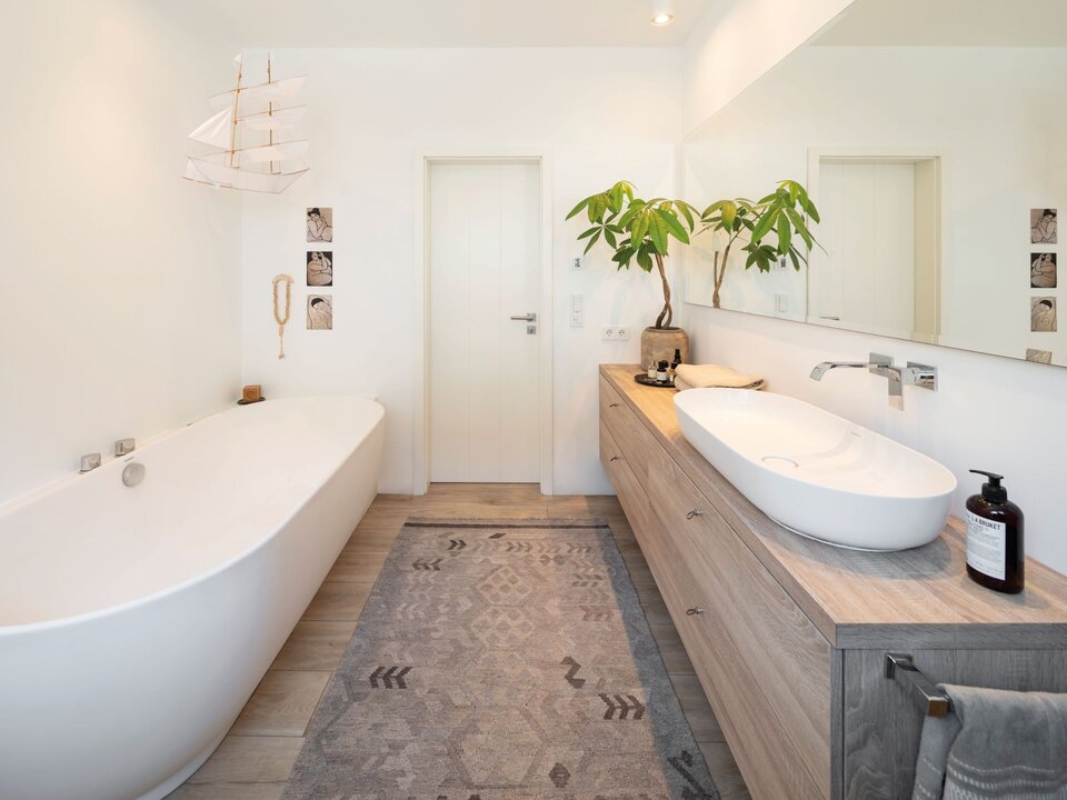 Modernes Badezimmer mit freistehender Badewanne, großem Waschtisch, langem Spiegel, Pflanzen und hellen Wänden.