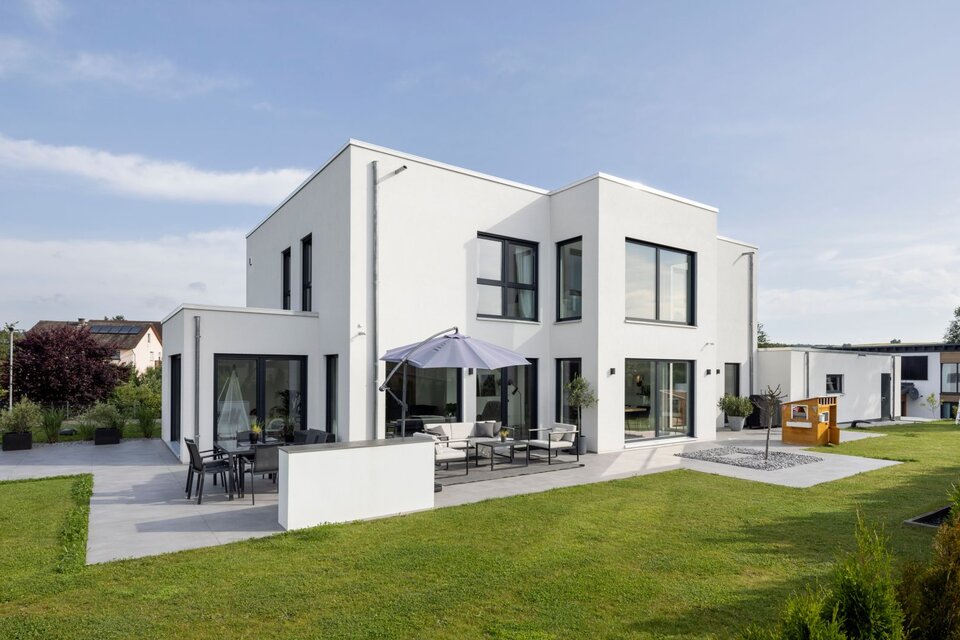 Moderne Außenansicht eines frei geplanten FingerHaus im Bauhaus-Stil. Kubische Architektur mit klaren Linien, großen Fensterflächen, Terrasse mit Sitzbereich und gepflegtem Garten.
