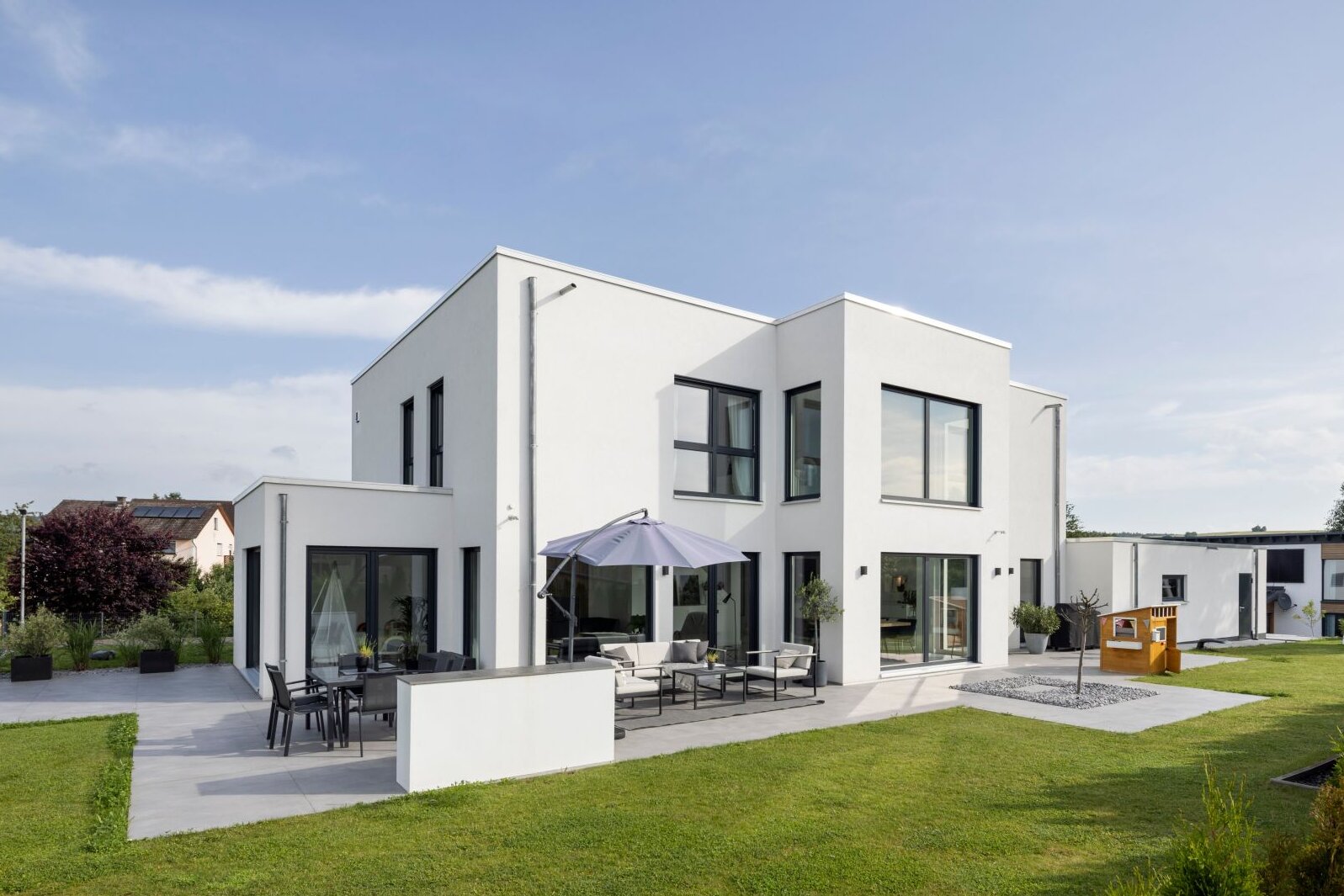 Moderne Außenansicht eines frei geplanten FingerHaus im Bauhaus-Stil. Kubische Architektur mit klaren Linien, großen Fensterflächen, Terrasse mit Sitzbereich und gepflegtem Garten.