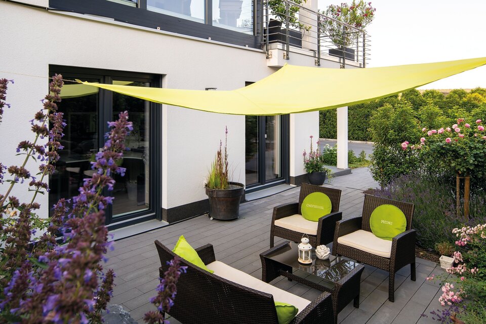 Moderne Terrasse mit Sitzgruppe, Sonnensegel und blühender Bepflanzung an einem stilvollen Flachdachhaus.