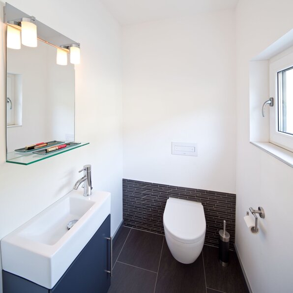 Modernes Gäste-Bad in einem frei geplanten FingerHaus mit Hänge-WC, kleinem Waschbecken, großem Spiegel und stilvollen dunklen Fliesen.