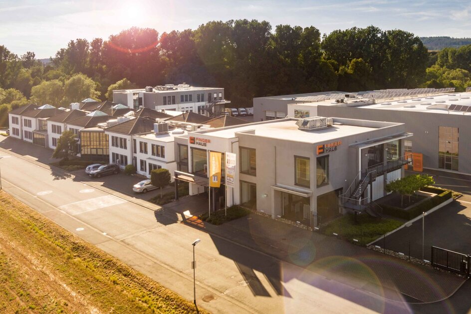 Luftaufnahme des Firmensitzes von FingerHaus in Frankenberg (Eder) bei Sonnenschein, mit Verwaltungsgebäude und Produktionshalle.