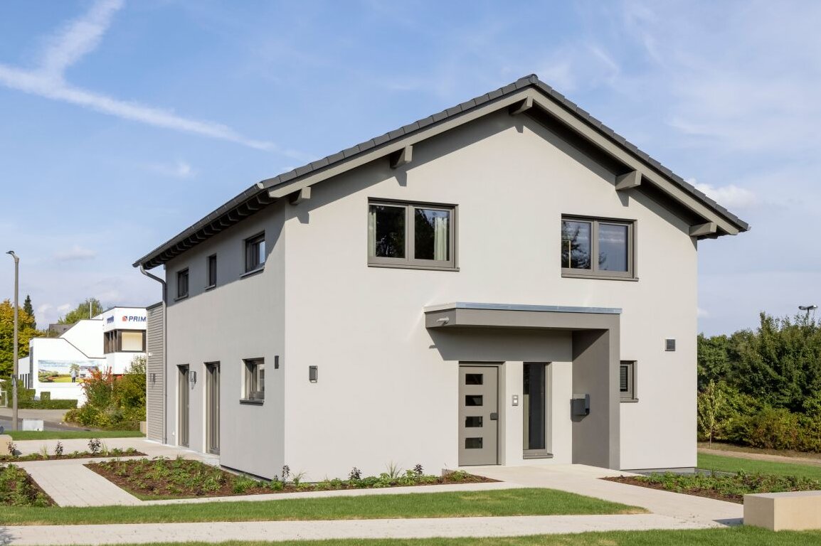 Außenansicht des FingerHaus ARTIS 300 Musterhauses Würzburg mit Eingangsüberdachung, grauer Fassade und gepflegtem Vorgarten.