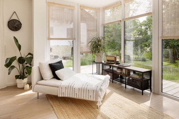 Heller Wohnbereich mit großer Fensterfront im FingerHaus, gemütlicher Liege, Teppich und modernen Naturmaterialien – mit Blick auf den Garten.
