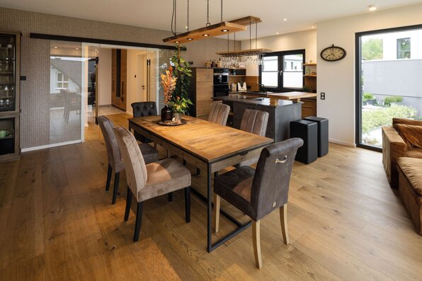 Frei geplantes FingerHaus mit stilvollem Essbereich und offener Küche, kombiniert mit warmen Holzakzenten.