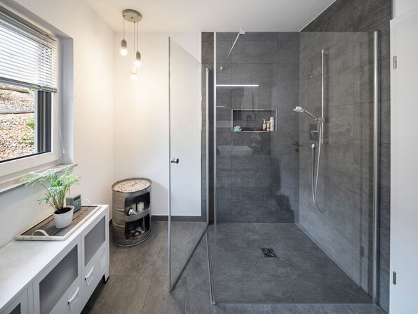 Badezimmer eines frei geplanten Kundenhauses mit bodengleicher Dusche und Glasduschwand.