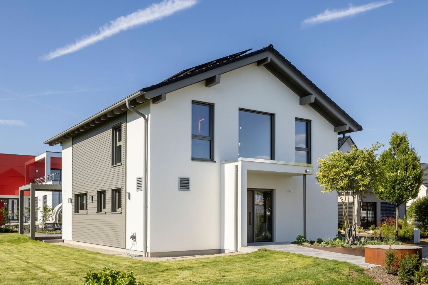 Modernes FingerHaus ARTIS 300 in Nürnberg mit Satteldach, weißer Fassade, grauen Akzenten und gepflegtem Garten bei sonnigem Wetter.