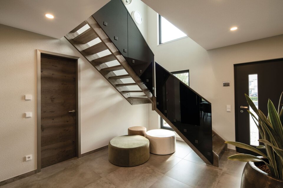 Moderner Flur mit Holztreppe, Sitzhockern und großen Fensterflächen im FingerHaus ALTERO, Musterhaus Gießen.