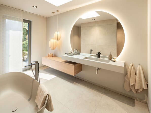 Badezimmer im FingerHaus Musterhaus NIVO in Frankenberg mit freistehender Badewanne, Doppelwaschtisch und großem rundem Spiegel.