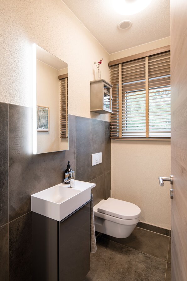 Modernes Gäste-WC im Musterhaus MEDLEY in Fellbach mit wandhängendem WC, Waschbecken und stilvollen Fliesen.