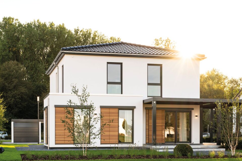 Außenansicht des Musterhauses MEDLEY 300 B in Frankenberg bei Sonnenuntergang mit modernen Fensterflächen und Holzlamellen.