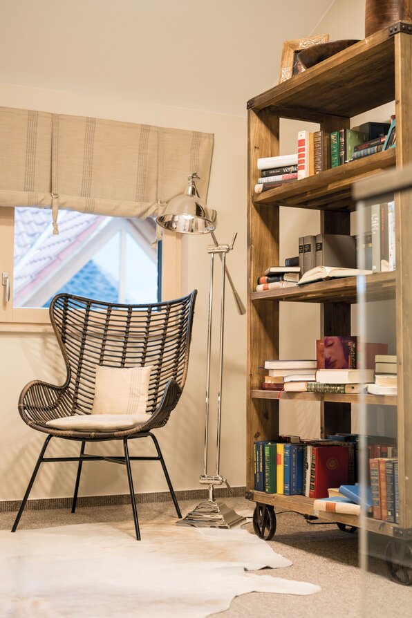 Gemütliche Leseecke im Musterhaus MEDLEY Fellbach mit Rattanstuhl, Stehlampe und Bücherregal.