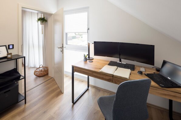 Homeoffice im Obergeschoss des FingerHaus SENTO 403 mit Holzschreibtisch, zwei Monitoren, Laptop und Fenster unter Dachschräge