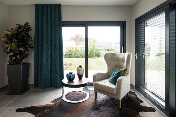 Heller Wohnbereich der Einliegerwohnung im Musterhaus ALTERO in Gießen mit Sessel, dekorativem Teppich und Zugang zur Terrasse.