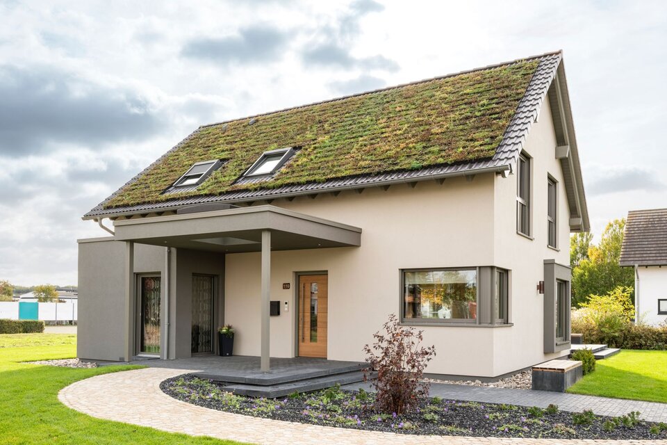 Modernes Musterhaus JUNO 300 in Mülheim-Kärlich mit begrüntem Satteldach, klarer Architektur und überdachtem Eingangsbereich.