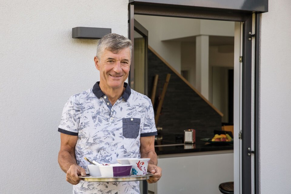 Mann steht mit einem Tablett voller Geschirr in der geöffneten Terrassentür eines modernen, frei geplanten FingerHaus-Hauses.