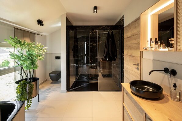 Modernes Badezimmer im FingerHaus ARTIS 300 Musterhaus Nürnberg mit schwarzer Dusche, Aufsatzwaschbecken und stilvoller Holzausstattung.