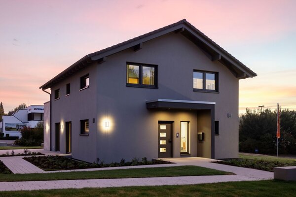 Musterhaus ARTIS 300 in Würzburg bei Abenddämmerung: Modernes zweigeschossiges Fertighaus mit klarer Architektur, beleuchtetem Eingangsbereich und gepflegtem Garten.