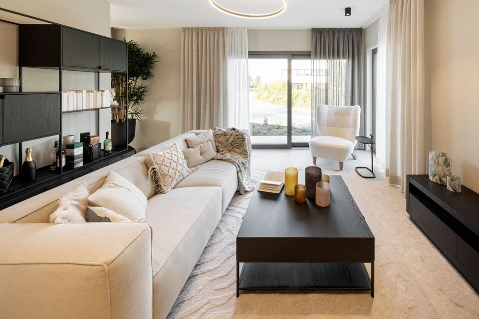 Helles Wohnzimmer im FingerHaus ARTIS 300 Musterhaus Würzburg mit beiger Couch, modernem Couchtisch und großen Fensterfronten.