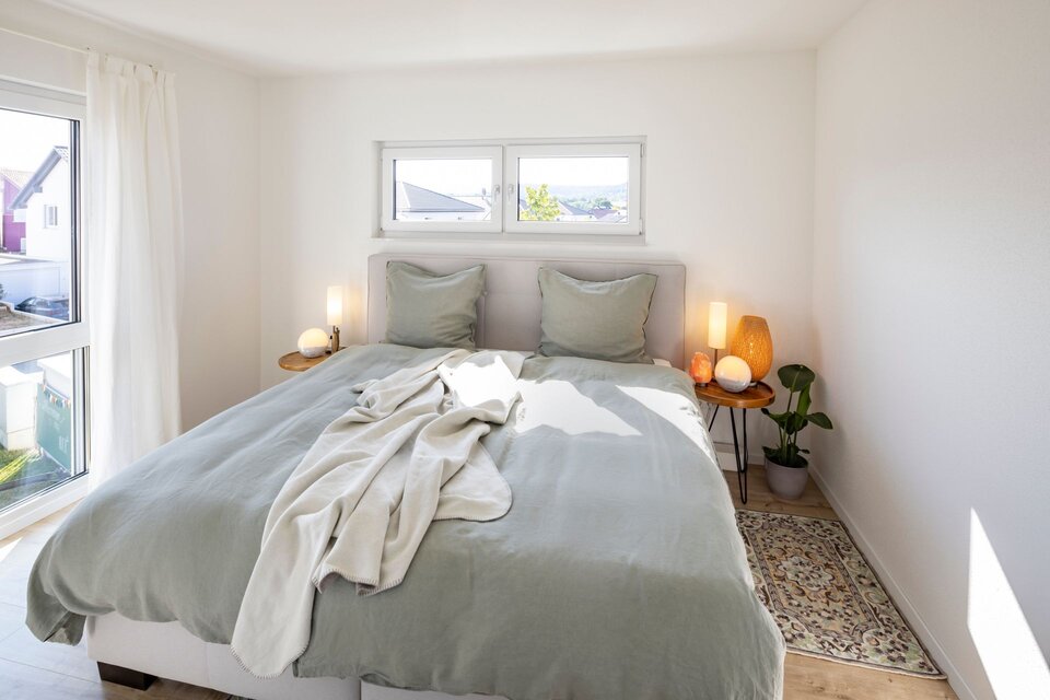 Helles Schlafzimmer im Obergeschoss eines FingerHaus MEDLEY 300 B mit großem Doppelbett, geraden Wänden ohne Dachschrägen und viel Tageslicht durch zwei Fensterfronten.