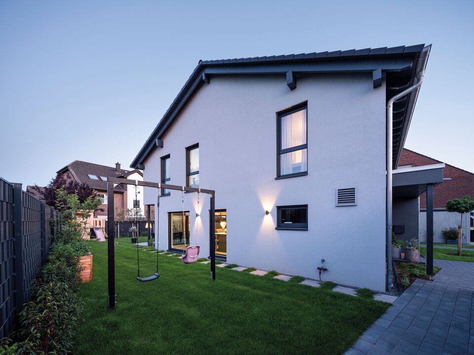 Doppelhaushälfte mit Satteldach und Garten mit Schaukelgestell und Rasenfläche neben der Hausfassade