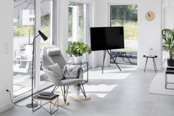 Helles Wohnzimmer mit modernem Schaukelstuhl, großen Fensterfronten und Zugang zur Terrasse. Minimalistische Einrichtung mit gemütlicher Leseecke.
