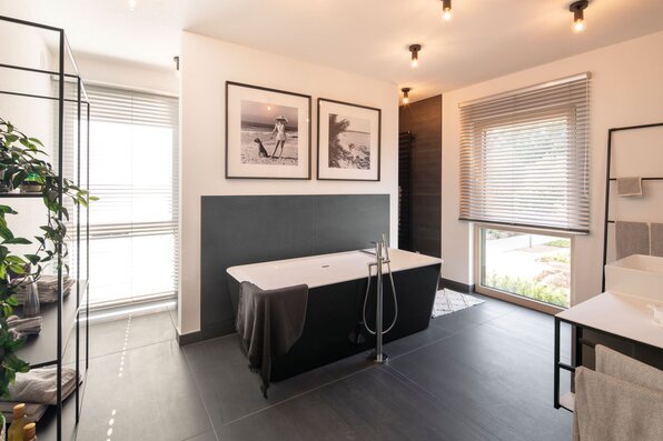 Helles Badezimmer im Musterhaus MEDLEY 300 B in Frankenberg mit freistehender Badewanne, großen Fenstern und modernem Interieur.