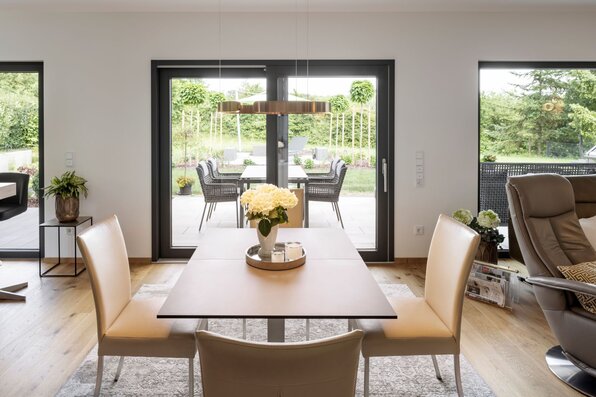 Moderner Essbereich in einem frei geplanten FingerHaus mit großem Esstisch, bequemen Lederstühlen und Blick durch bodentiefe Fenster auf die Terrasse und den Garten.