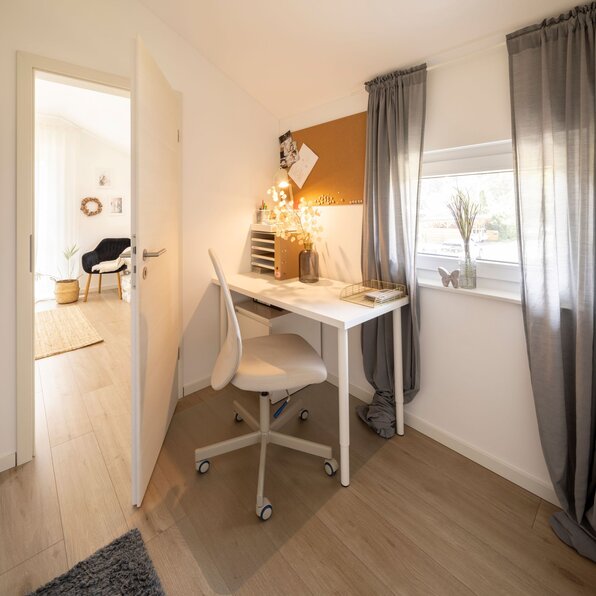 Kleines, helles Büro im frei geplanten FingerHaus mit Schreibtisch am Fenster und gemütlicher Atmosphäre.