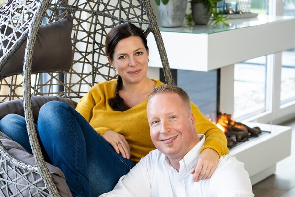 Ein Paar sitzt entspannt vor dem Kamin im modernen Wohnbereich ihres FingerHaus – sie in einem Hängesessel, er auf dem Boden davor.