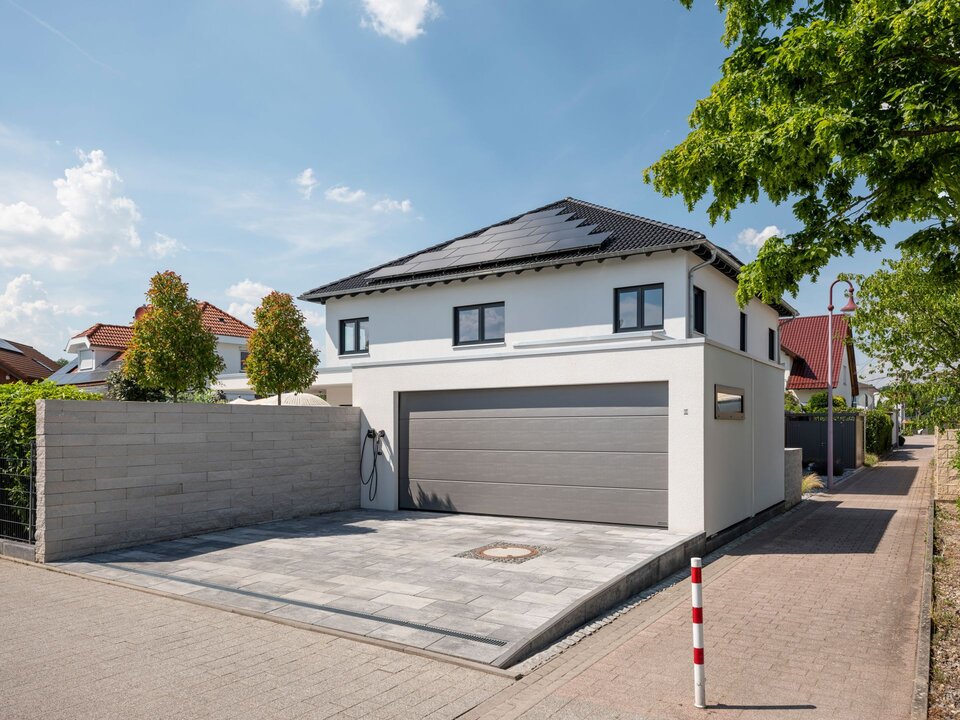 Vorderansicht einer modernen Stadtvilla mit Doppelgarage, Einfahrt und Grundstücksmauer.