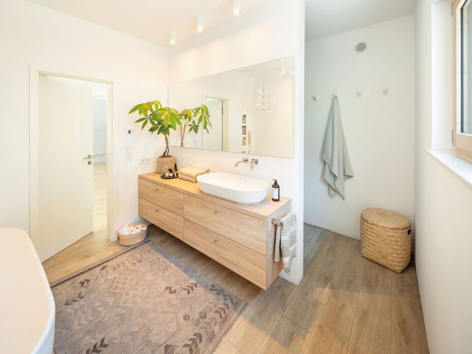 Helles Badezimmer mit großem Waschtisch aus Holz, modernem Aufsatzwaschbecken, großem Spiegel, Pflanzen und hellem Design.