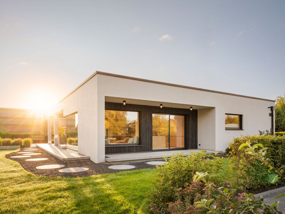 FingerHaus Musterhaus NIVO in Frankenberg, moderner Bungalow mit Flachdach, weißer Fassade und überdachter Terrasse im Abendlicht.