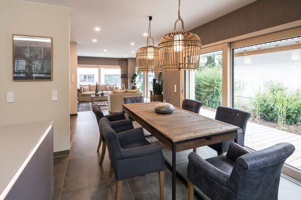 Essbereich im Musterhaus MEDLEY in Fellbach mit Holztisch, Polsterstühlen und großen Fenstern zum Garten.