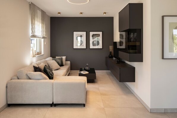 Wohnzimmer im FingerHaus ARTIS 300 Musterhaus Nürnberg mit heller Eckcouch, dunkler Akzentwand und modernem TV-Möbel.