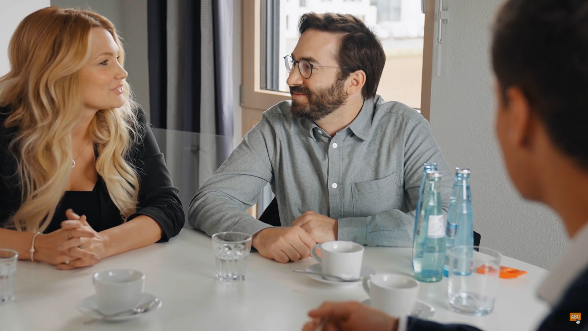 Thumbnail eines Expertenvideos von FingerHaus, ein Fachberater im Gespräch mit einem Paar an einem Tisch mit Unterlagen und Wasserflaschen.