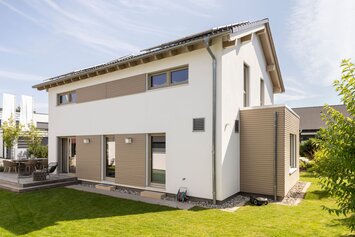 Moderne Rückansicht des Musterhauses MEDLEY 300 B in Poing mit großer Terrasse, gepflegtem Garten und klarer Linienarchitektur.