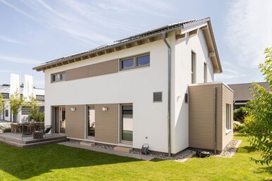 Moderne Rückansicht des Musterhauses MEDLEY 300 B in Poing mit großer Terrasse, gepflegtem Garten und klarer Linienarchitektur.