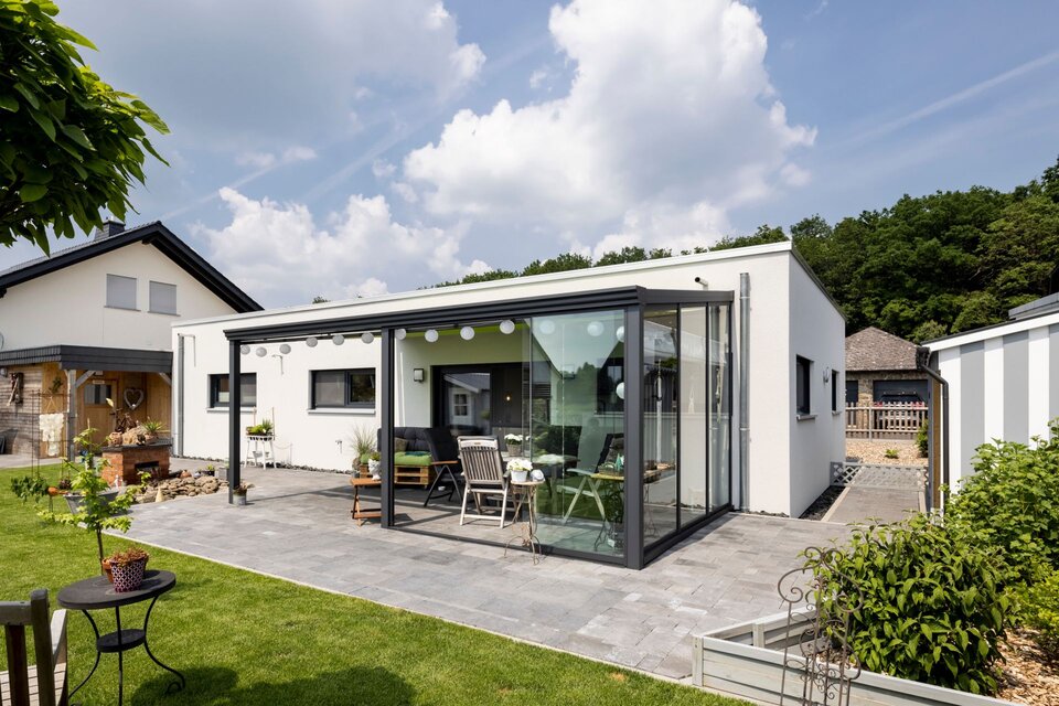 Modernes eingeschossiges Flachdachhaus mit verglaster Terrasse, gepflastertem Gartenbereich und Sitzmöbeln bei Tageslicht