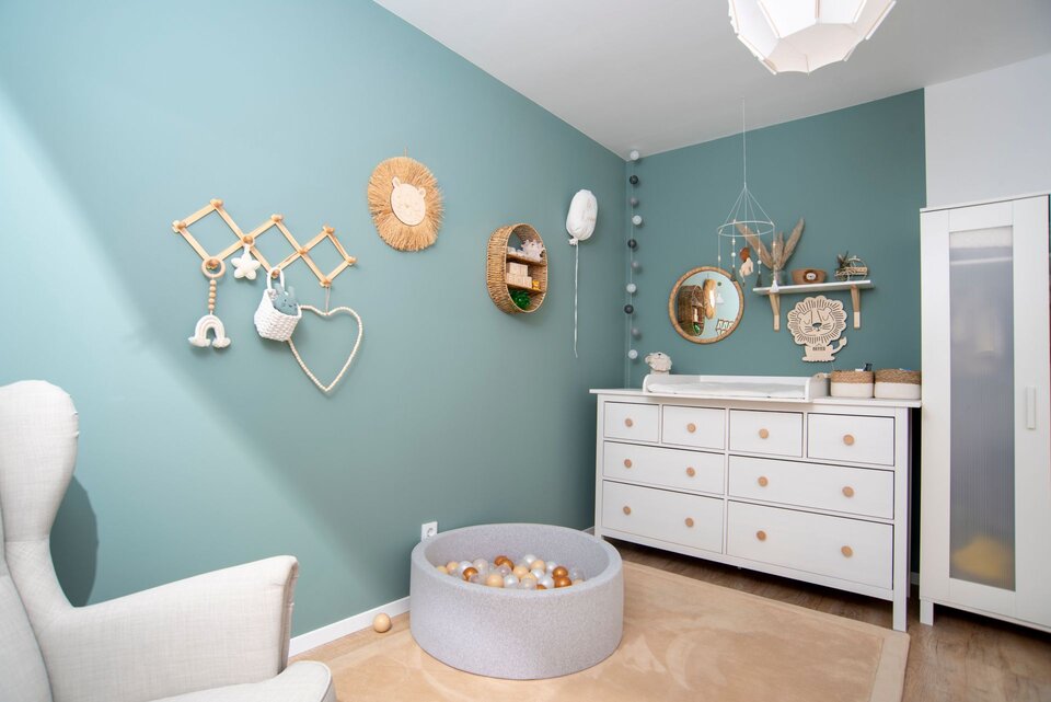 Kinderzimmer mit türkisfarbener Akzentwand, dekorativen Wandhängern, weißer Kommode und rundem Spielbett.