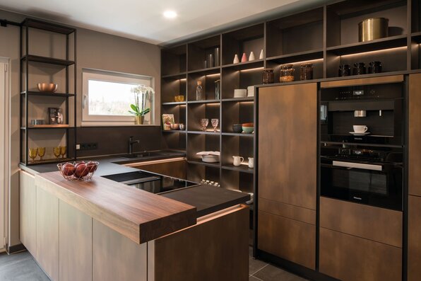 Designerküche im FingerHaus MEDLEY 300 B Musterhaus Kassel mit modernen Einbaugeräten, offenen Regalen und eleganter Holzarbeitsfläche.