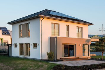 Rückansicht des Musterhauses MEDLEY 300 B in Kassel mit klarer Architektur, großen Fensterflächen und FingerHaus-Flagge im Vordergrund.