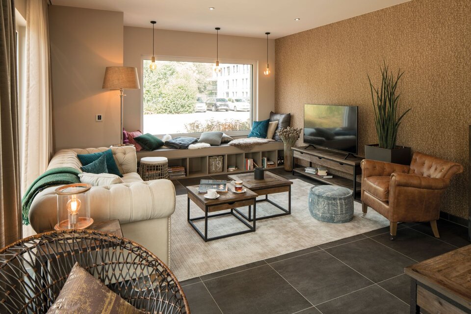 Gemütliches Wohnzimmer im FingerHaus SENTO 500 Musterhaus Frankenberg mit heller Eckcouch, TV-Bereich, Fensterbank-Sitzplatz und stilvoller Einrichtung in warmen Farben.