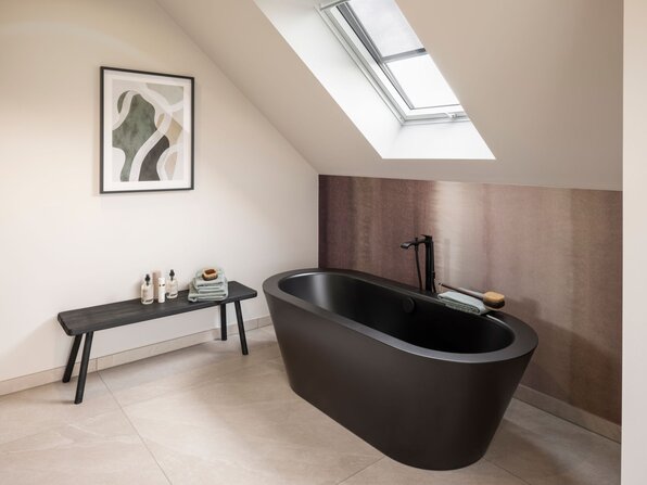 Modernes Badezimmer im Dachgeschoss des Musterhauses JUNO 300 in Mülheim-Kärlich mit freistehender schwarzer Badewanne unter Dachschräge.